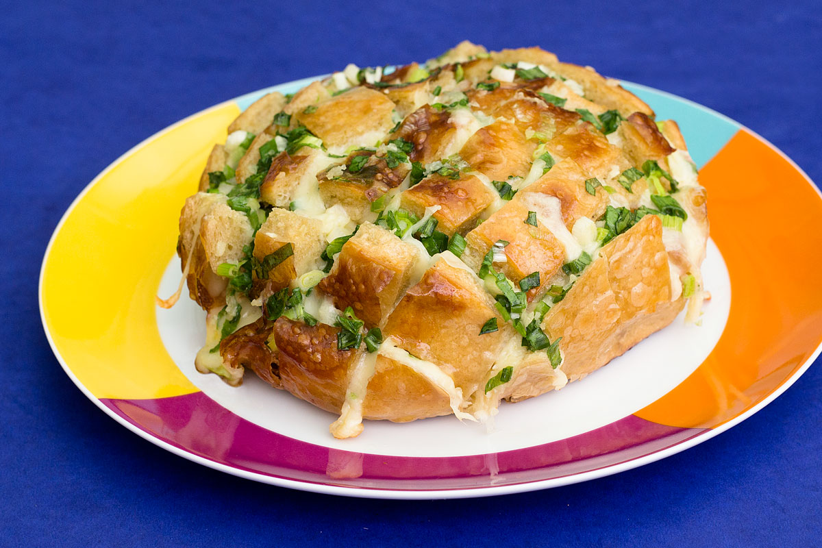 Foto do pão italiano com queijo recheado com manteiga, alho e cebolinha.